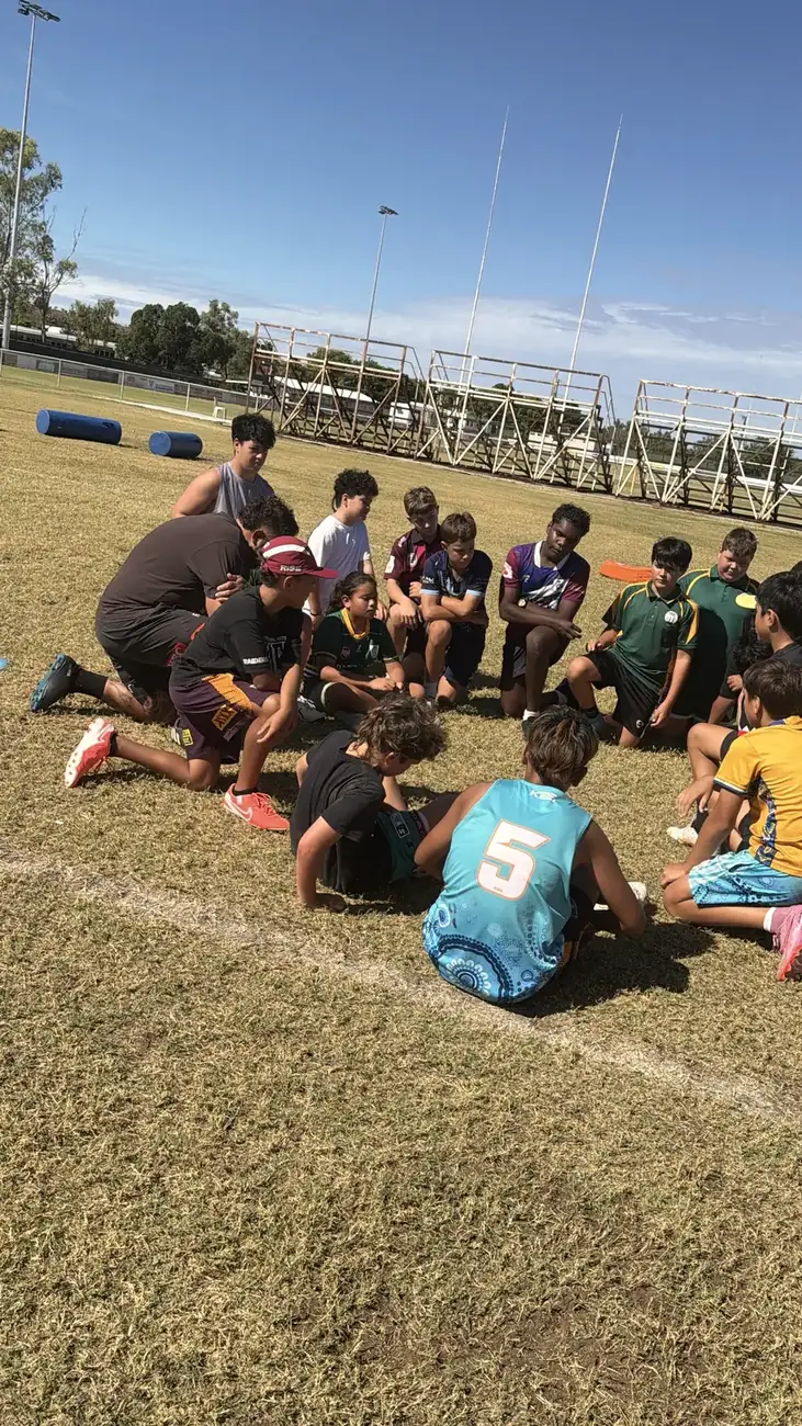 Young people kneeling in a circle for a team talk on the field