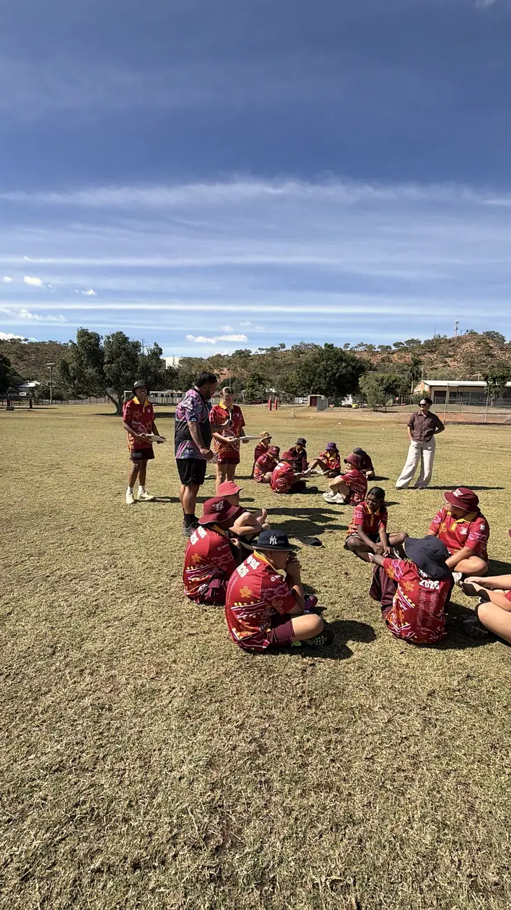 Students sitting in a circle on the grass with the red hills behind them