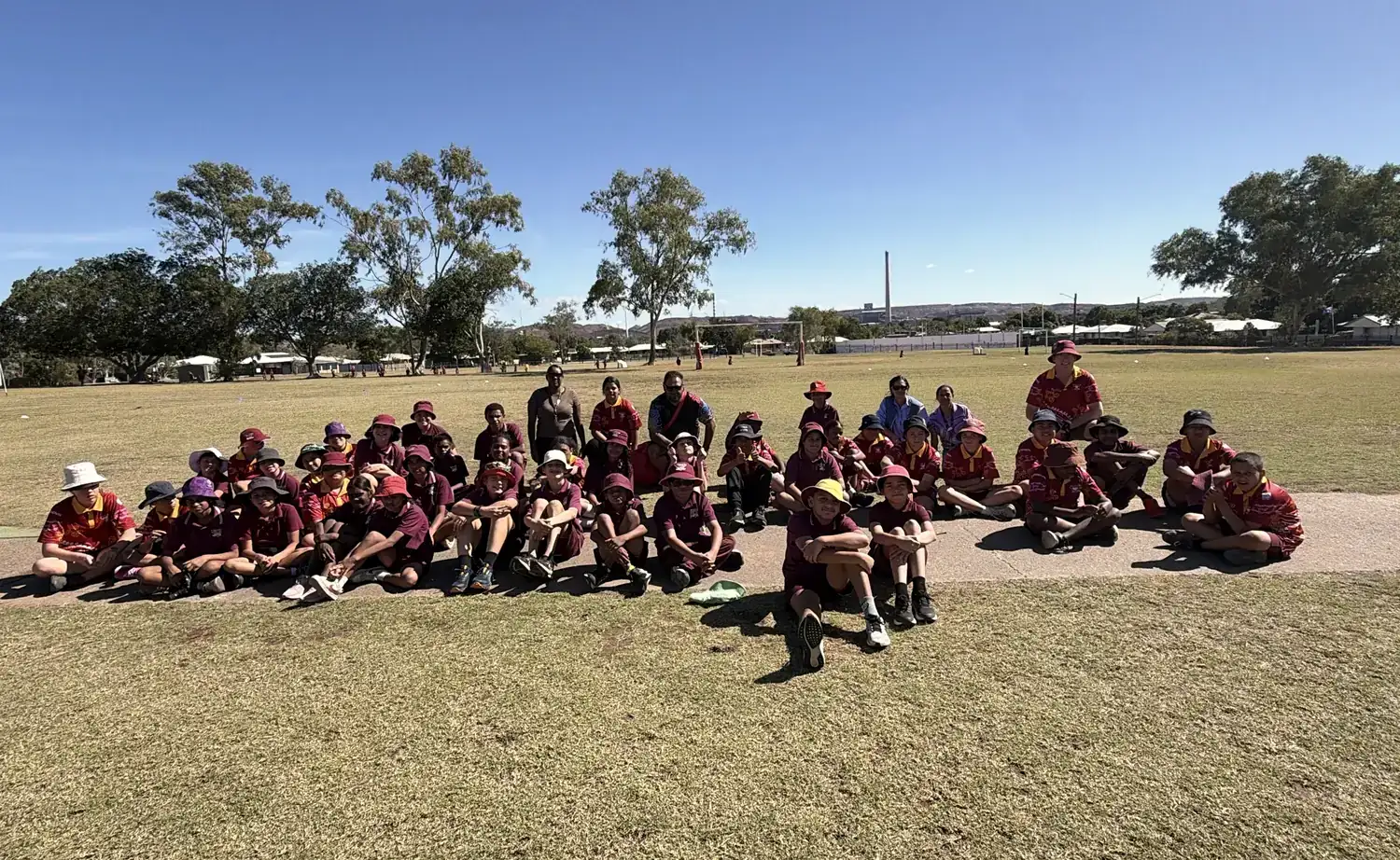 Students and staff sitting together on the school oval, with the Mount Isa stack in the distance