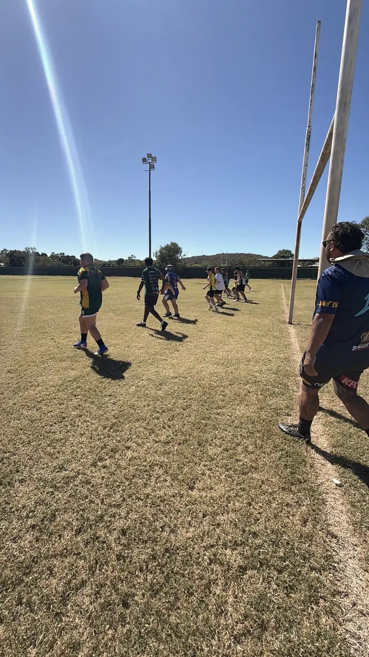 Players running a drill beside the goalposts with a coach watching