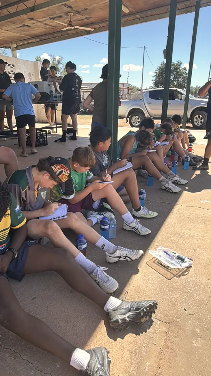 Players writing in journals in the shade after training